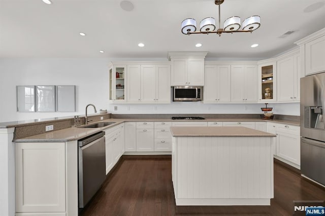 kitchen with a peninsula, glass insert cabinets, appliances with stainless steel finishes, and a sink