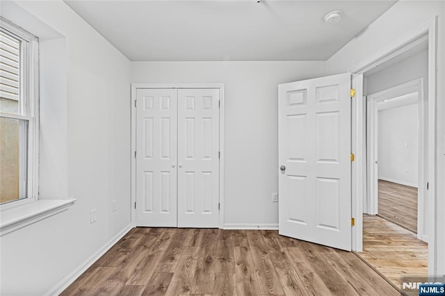 unfurnished bedroom featuring wood finished floors, baseboards, and a closet