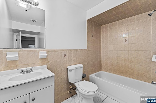 bathroom with visible vents, washtub / shower combination, toilet, vanity, and tile walls