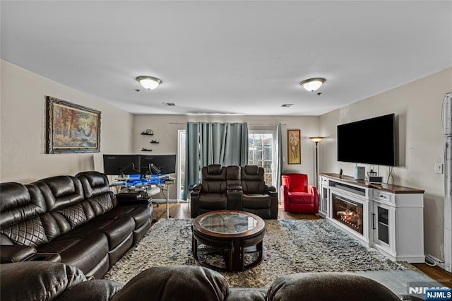 living area featuring a glass covered fireplace, wood finished floors, and visible vents