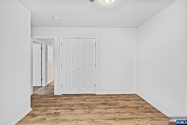 unfurnished bedroom featuring wood finished floors, a closet, and baseboards