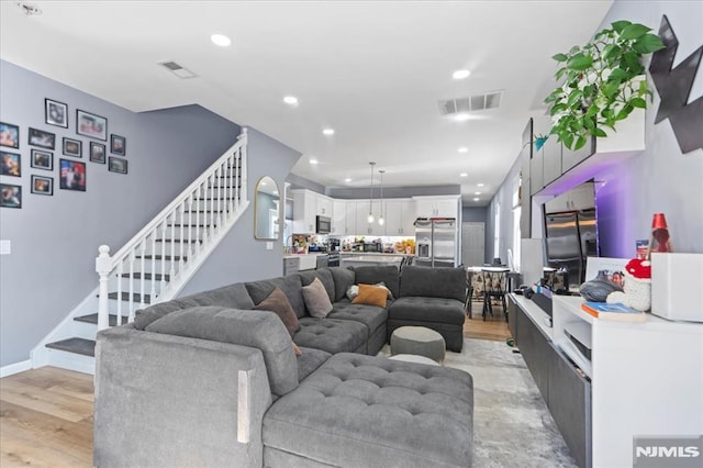 living area with visible vents, light wood-style flooring, and stairway