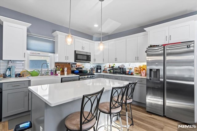 kitchen featuring light wood finished floors, a kitchen island, light countertops, stainless steel appliances, and a sink