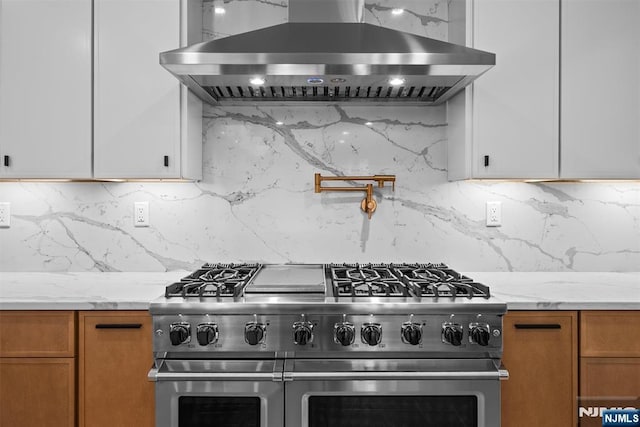 kitchen with brown cabinetry, light stone countertops, range with two ovens, island exhaust hood, and tasteful backsplash