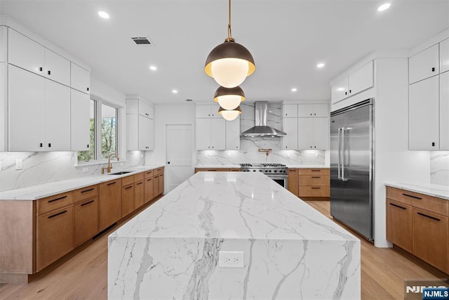 kitchen featuring tasteful backsplash, a center island, wall chimney range hood, high end appliances, and a sink