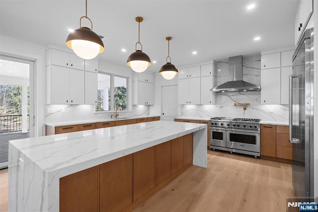 kitchen with range with two ovens, a healthy amount of sunlight, a sink, and wall chimney range hood