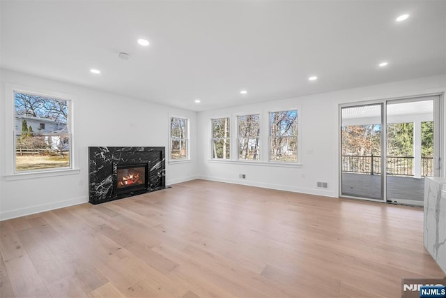 unfurnished living room featuring recessed lighting, a premium fireplace, plenty of natural light, and light wood finished floors