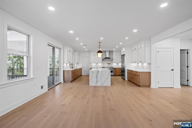 kitchen with brown cabinets, a sink, a center island, light wood-style floors, and wall chimney range hood