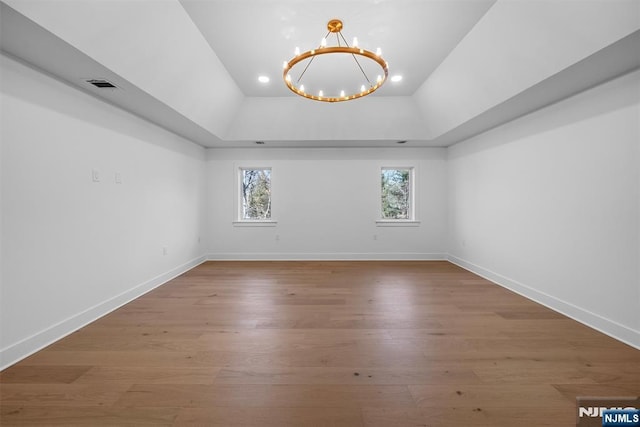 unfurnished room with an inviting chandelier, wood finished floors, baseboards, and a tray ceiling