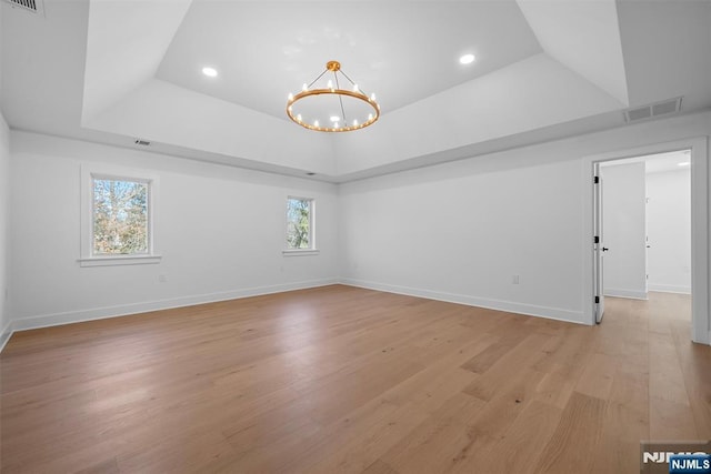 empty room featuring visible vents, a tray ceiling, light wood-style flooring, plenty of natural light, and a chandelier