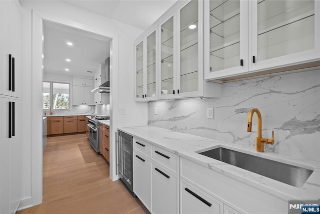 kitchen with high end stove, light stone countertops, beverage cooler, white cabinetry, and a sink