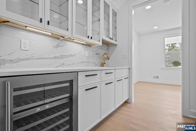 bar featuring beverage cooler, visible vents, light wood-style flooring, a sink, and tasteful backsplash