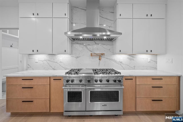 kitchen featuring double oven range, white cabinetry, wall chimney range hood, and light stone countertops