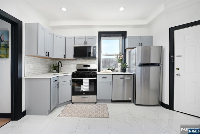 kitchen featuring light countertops, decorative backsplash, gray cabinets, appliances with stainless steel finishes, and marble finish floor