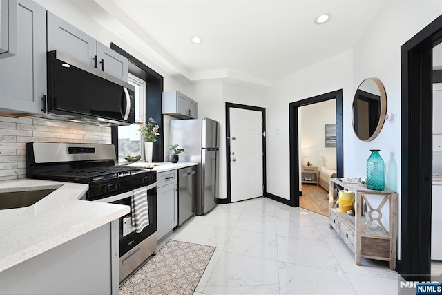 kitchen featuring marble finish floor, gray cabinetry, stainless steel appliances, decorative backsplash, and light stone countertops