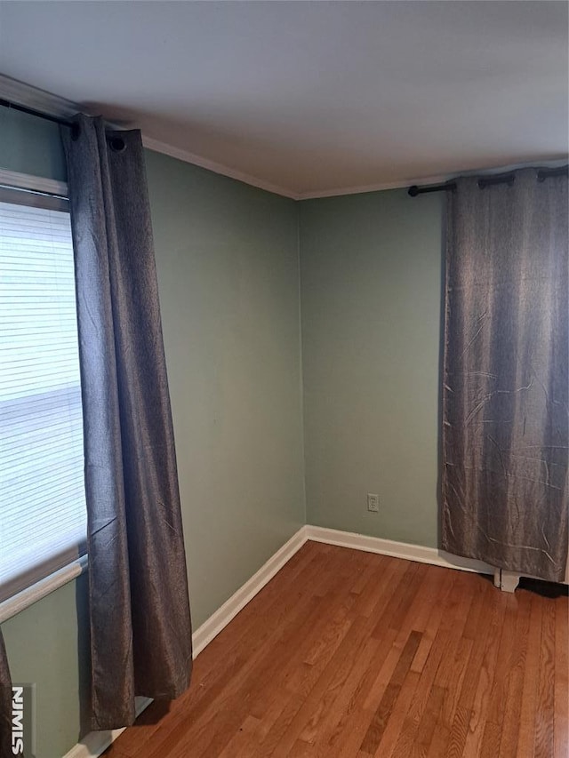 empty room with ornamental molding, baseboards, and wood finished floors