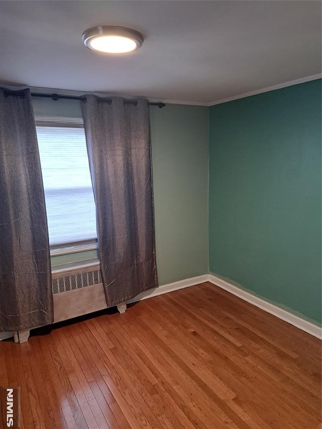 spare room featuring crown molding, baseboards, and wood finished floors