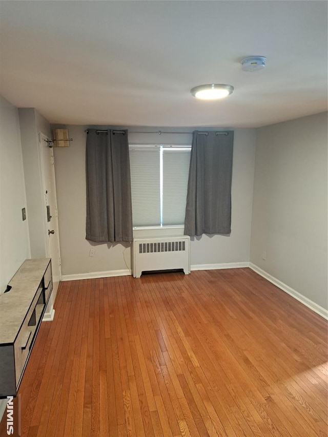 empty room with radiator, baseboards, and light wood-style floors