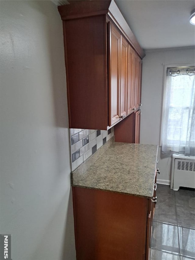 kitchen featuring tasteful backsplash, radiator, dark tile patterned floors, and brown cabinetry