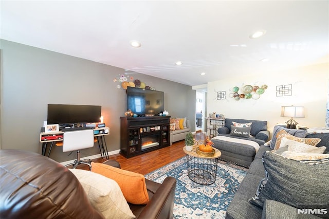 living room featuring a glass covered fireplace, baseboards, wood finished floors, and recessed lighting