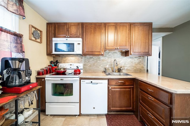 kitchen featuring brown cabinets, a sink, tasteful backsplash, white appliances, and a peninsula