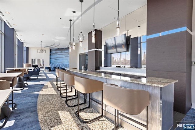 kitchen featuring light stone countertops, decorative light fixtures, open floor plan, a kitchen breakfast bar, and dark colored carpet