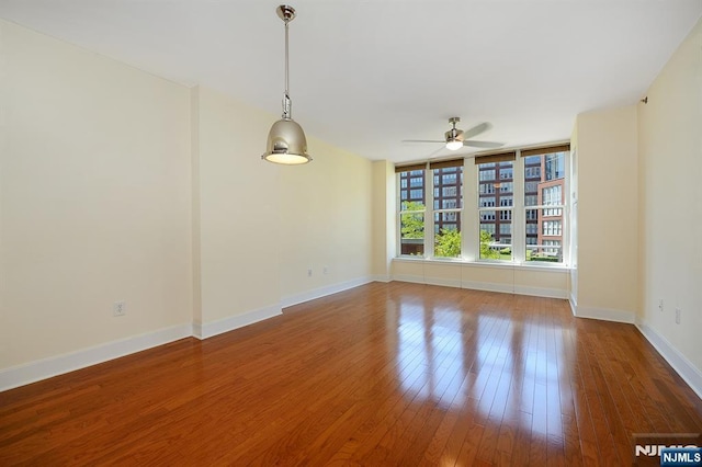 empty room with a ceiling fan, wood finished floors, and baseboards