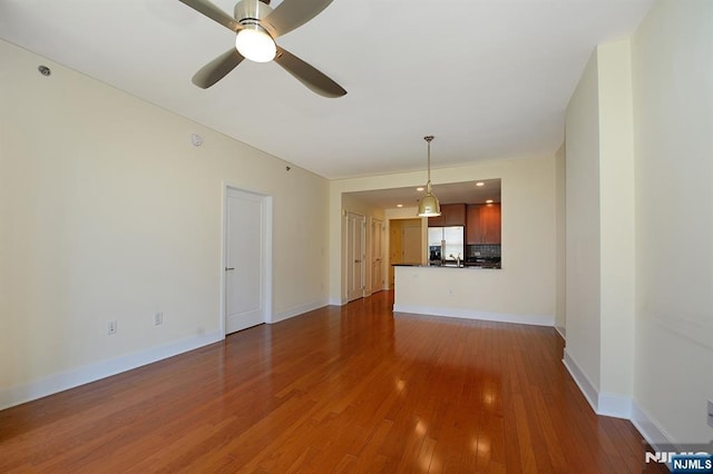 unfurnished living room with wood finished floors, baseboards, and ceiling fan