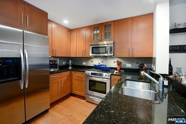 kitchen with a sink, stainless steel appliances, light wood-style flooring, and decorative backsplash