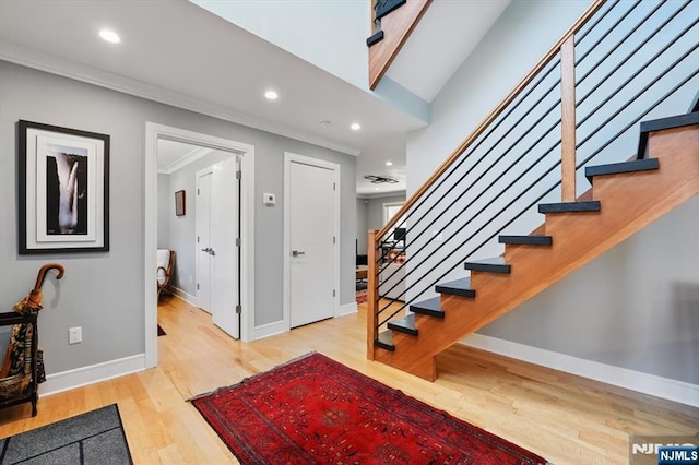 foyer featuring crown molding, wood finished floors, baseboards, and stairs