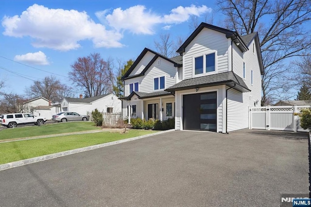 view of front of property with fence, an attached garage, aphalt driveway, a front lawn, and a gate