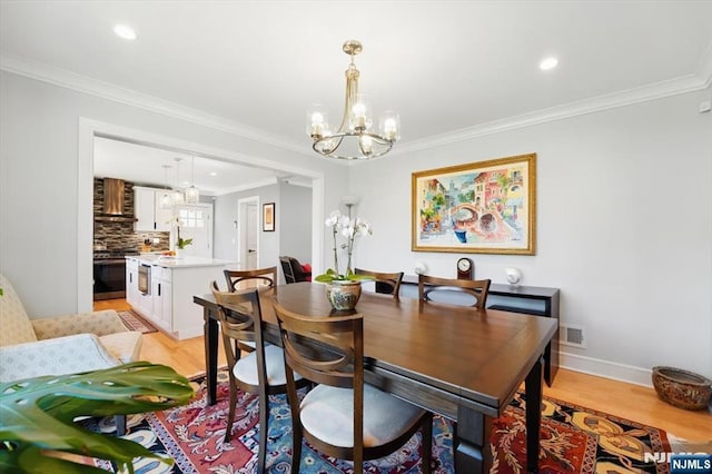 dining area with crown molding, light wood-type flooring, visible vents, and a notable chandelier
