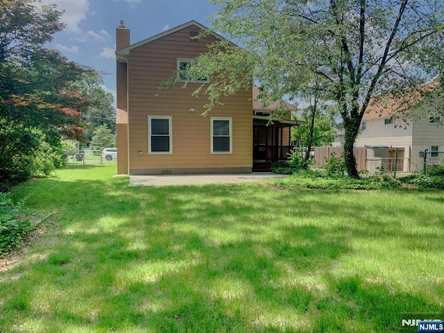 rear view of property with fence, a chimney, a yard, and a patio