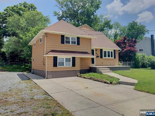 split level home featuring a front lawn, fence, and roof with shingles