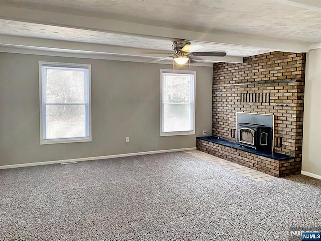 unfurnished living room with a wealth of natural light, carpet flooring, beam ceiling, and a wood stove