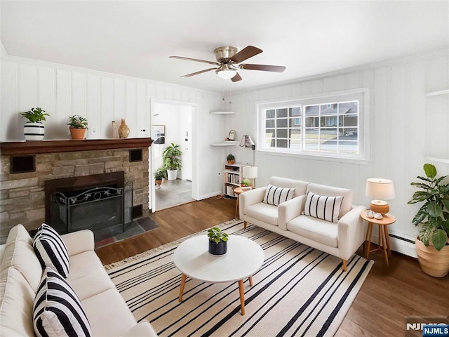 living room featuring a stone fireplace, wood finished floors, a baseboard heating unit, and a ceiling fan