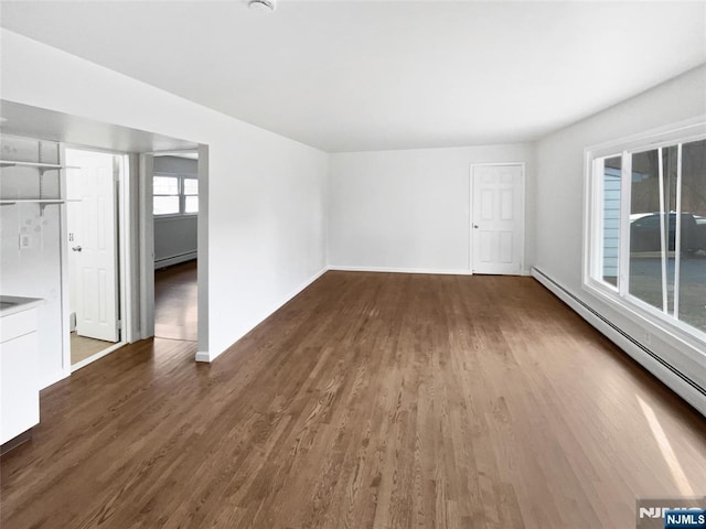 empty room with wood finished floors, baseboards, and a baseboard radiator