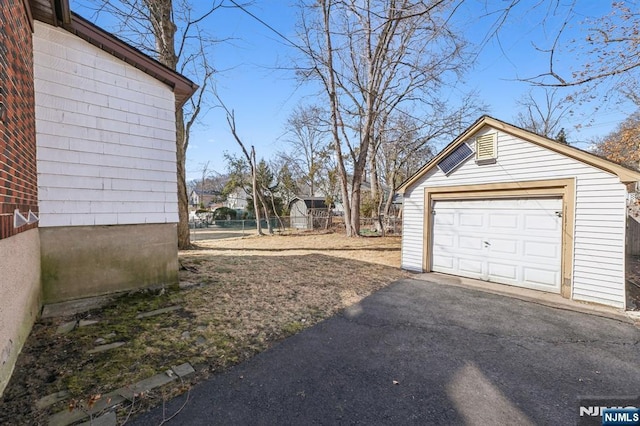 view of yard featuring driveway, a detached garage, an outdoor structure, and fence