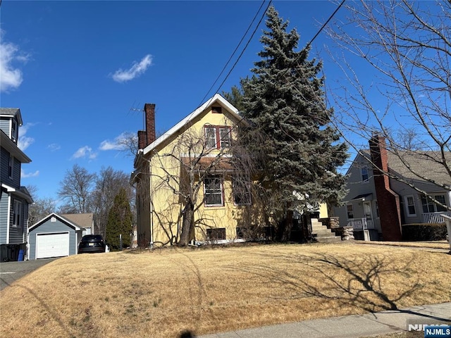 view of front of home featuring driveway, a front lawn, an outdoor structure, a garage, and a chimney