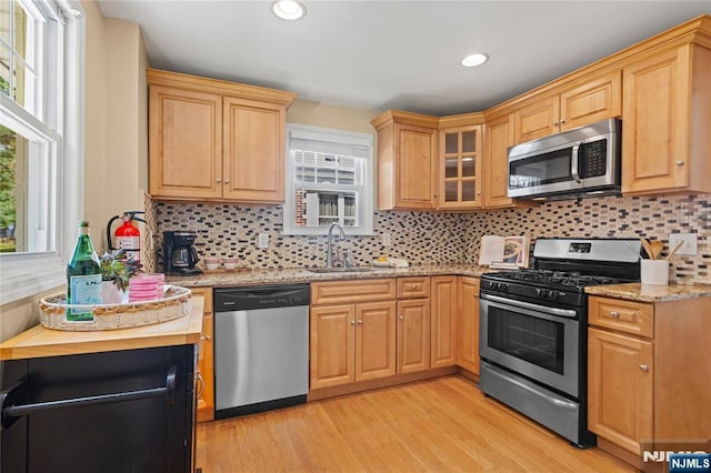 kitchen with light stone counters, a sink, light wood-style flooring, stainless steel appliances, and backsplash