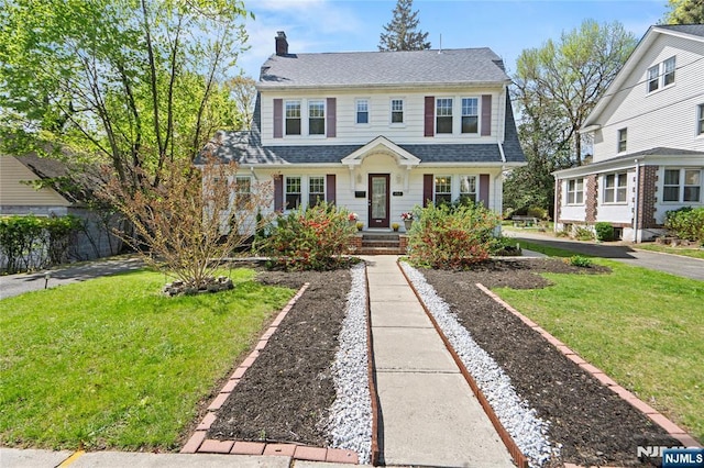 view of front of home featuring a chimney, a shingled roof, and a front yard