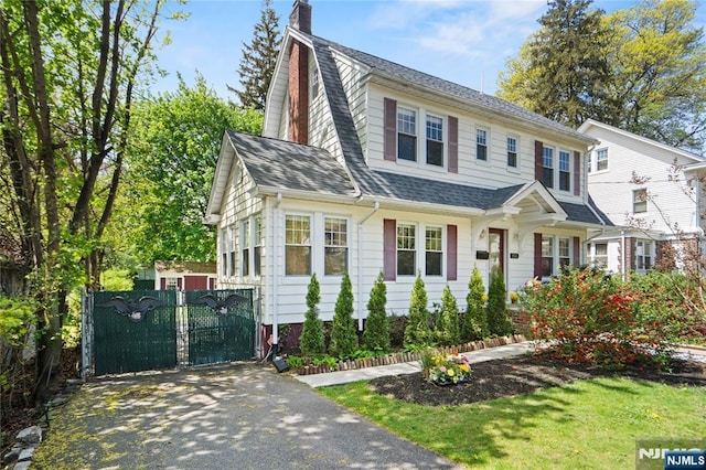view of front of property featuring roof with shingles, a gate, a chimney, and fence