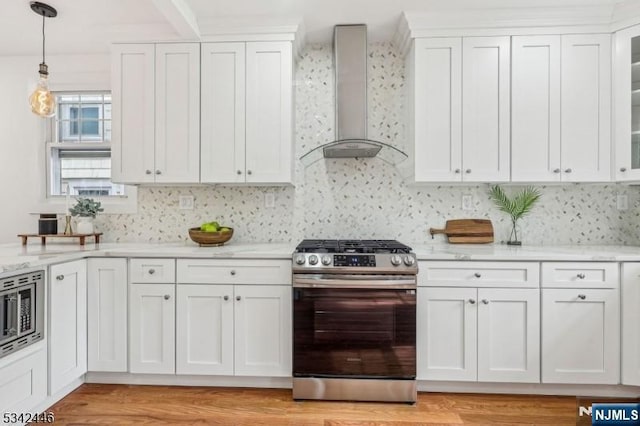 kitchen featuring white cabinetry, wall chimney range hood, glass insert cabinets, and stainless steel appliances