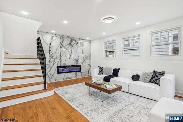 living room with an accent wall, stairway, recessed lighting, a fireplace, and wood finished floors