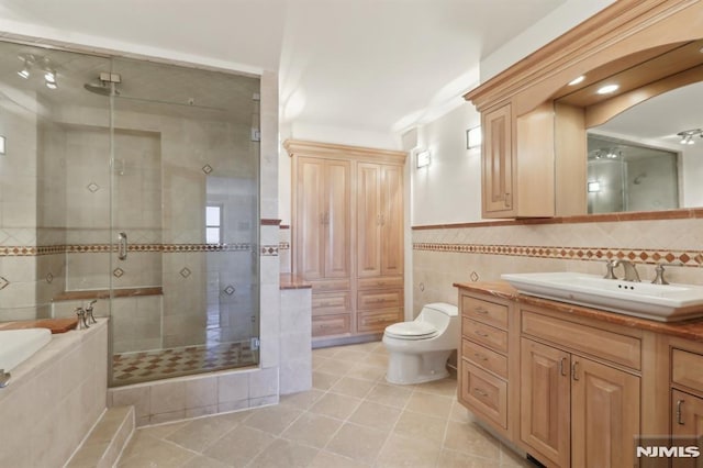 full bathroom with tile patterned flooring, toilet, vanity, a stall shower, and tile walls