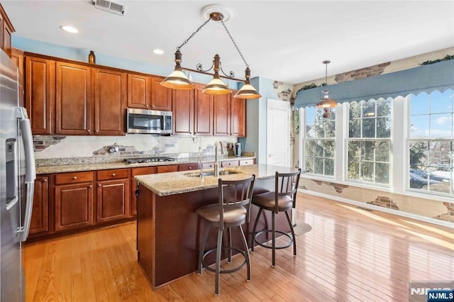 kitchen featuring visible vents, light stone counters, a sink, stainless steel appliances, and light wood-style floors