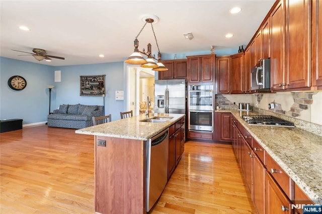 kitchen with light stone counters, light wood-style flooring, stainless steel appliances, and a sink