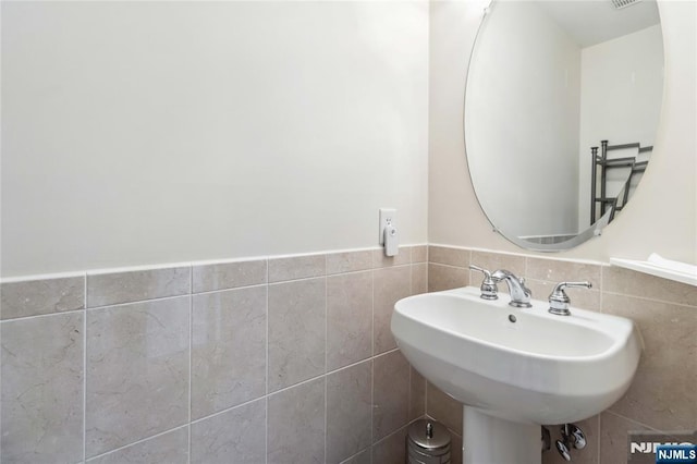 bathroom featuring a wainscoted wall, tile walls, and a sink