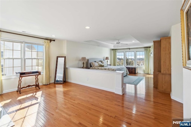 bedroom featuring a raised ceiling, recessed lighting, light wood-type flooring, and baseboards