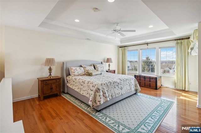 bedroom featuring recessed lighting, baseboards, a tray ceiling, and wood finished floors